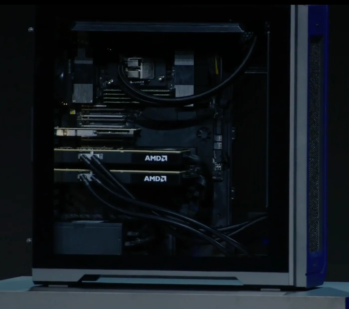Close-up through the glass side panel of the Threadripper Halo Station. Two accelerator cards are mounted horizontally one above the other, each with liquid cooling lines attached, beneath a smaller card in the topmost slot and a liquid-cooled processor block above that. Two accelerators are visible and no others are installed.