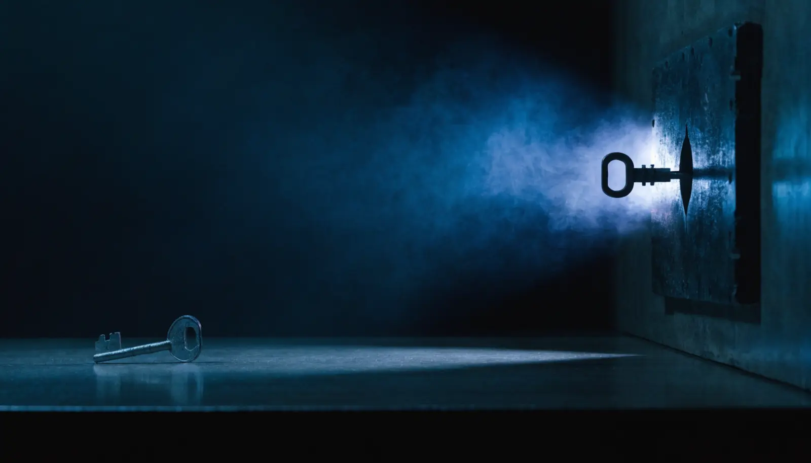 An illustration of a key lying alone and brightly lit on an empty surface at the left, and to the right an identical key seated and turned in a keyway set into a dark wall, with light spilling from behind the plate.