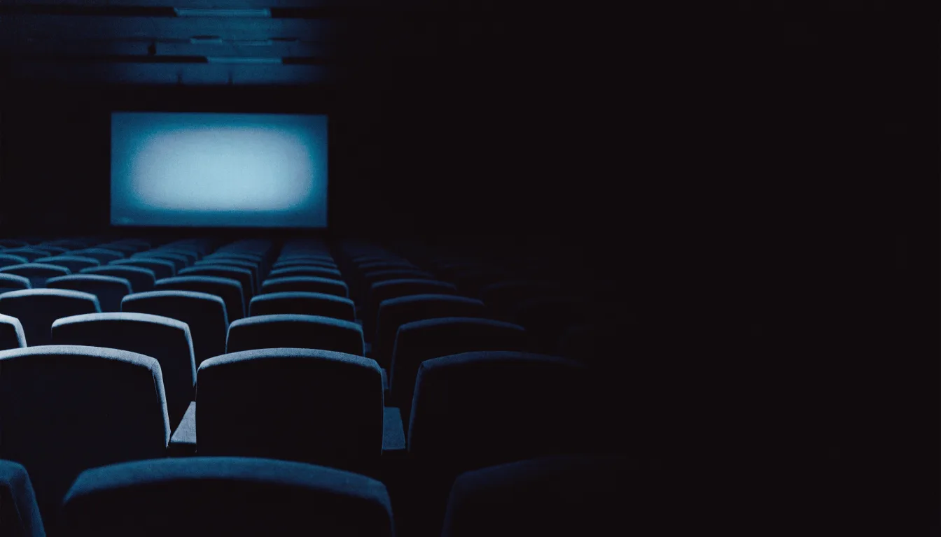 An empty lecture room at night with rows of seats in shadow and a cyan-lit screen at the front