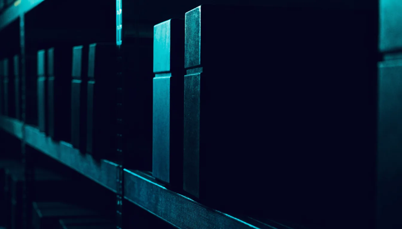 Rows of dark equipment cases on steel shelving receding into shadow, one pulled forward under cyan light