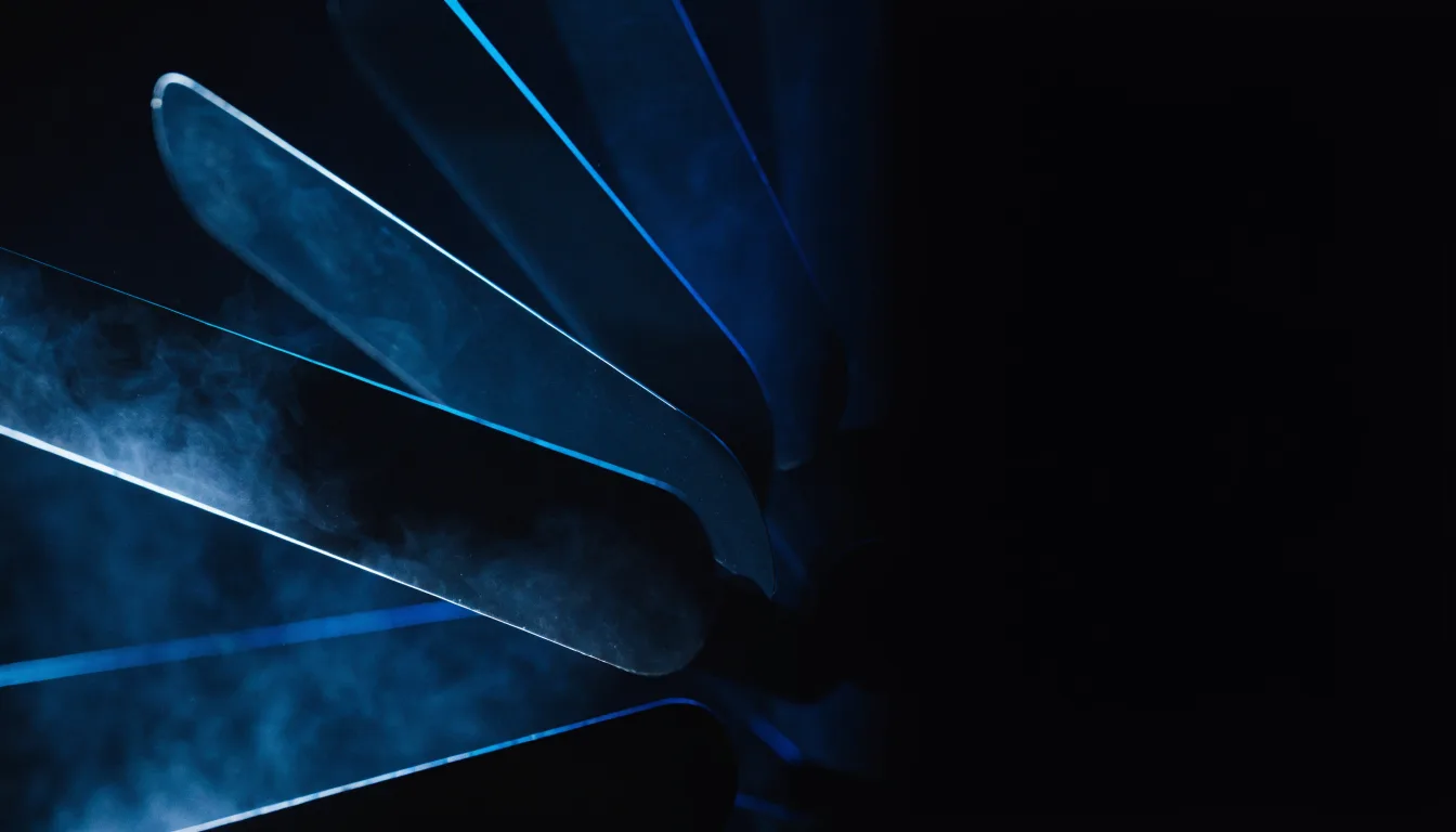 Angled blades of a split-flap display caught mid-turn in deep shadow, edges lit indigo and cyan, with no characters legible