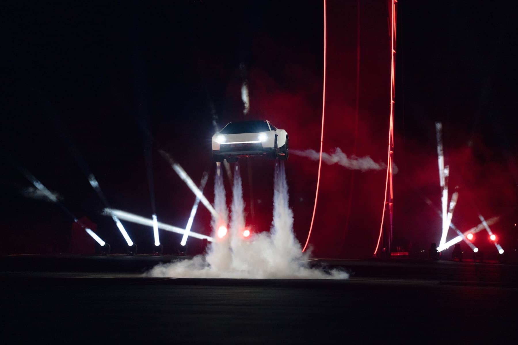 White Tesla Roadster prototype airborne above the demonstration site, with cold-gas plumes beneath it at night.