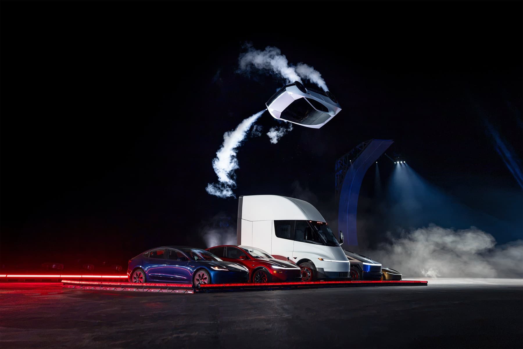 Roadster inverted above several Tesla vehicles during a night-time show.
