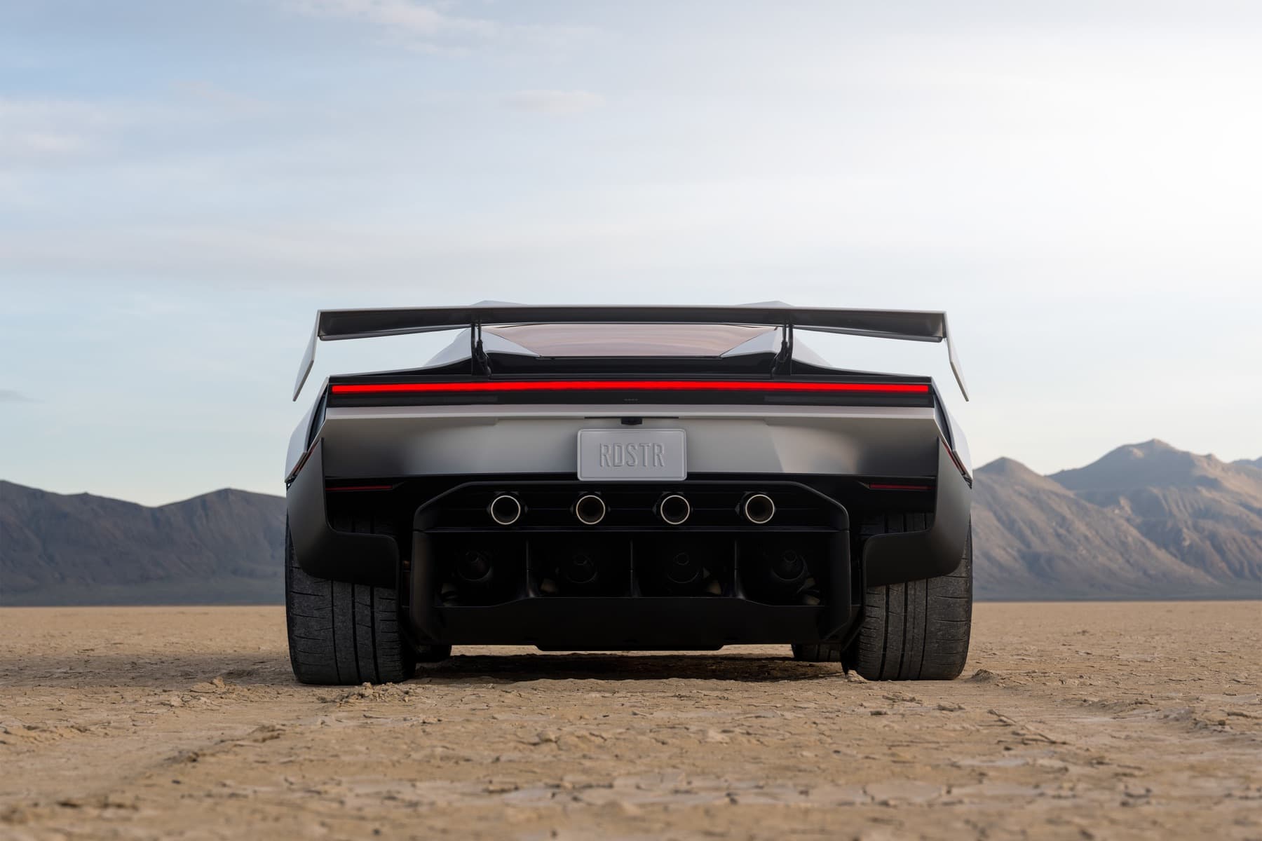 Rear of white Roadster showing a wide wing and four circular nozzle openings.