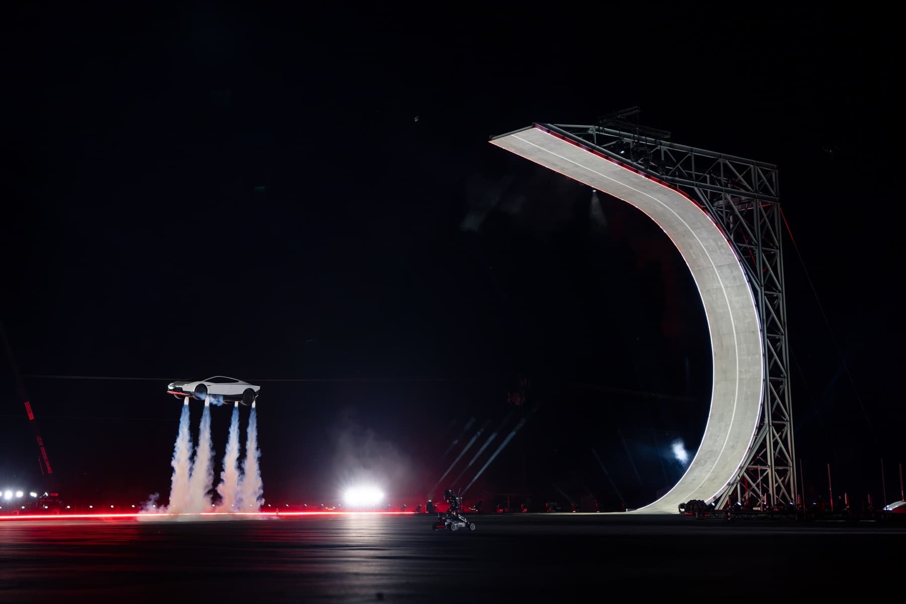 Wide night view of the white Roadster airborne beside the large curved ramp.